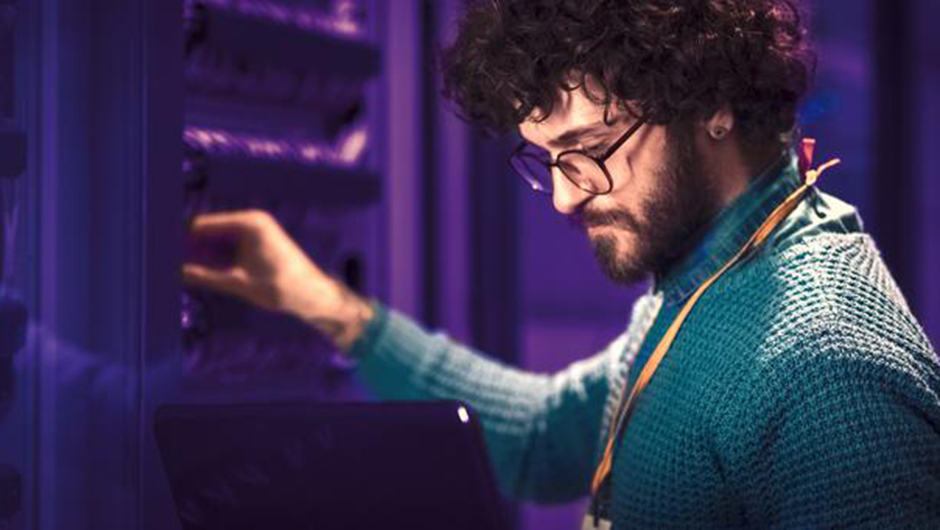 Image of a man holding the right hand on a server and looking at the laptop