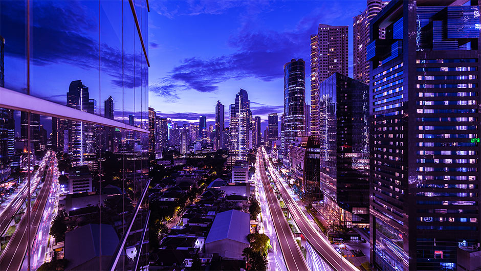 Jakarta city skyline at dusk with illuminated skyscrapers and vibrant urban lights.