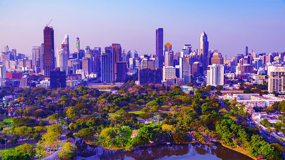 Bangkok city skyline with lush green park in the foreground under a clear blue sky.