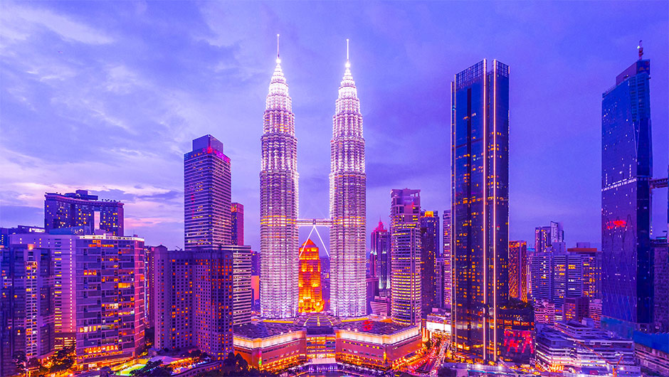 Kuala Lumpur skyline at dusk featuring the illuminated Petronas Twin Towers and modern skyscrapers.