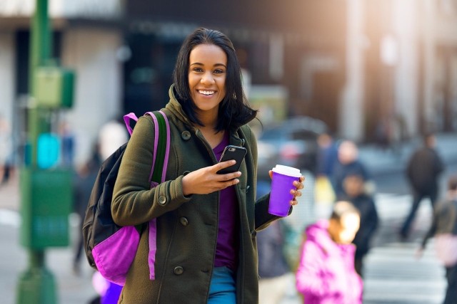 Image of girl with phone in hand and coffee in busy street