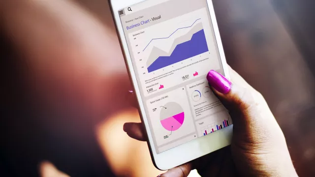Image of hand holding a mobile phone with graphs on display