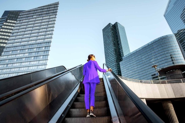 Image of woman in escalator with buildings in the background