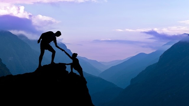 Image of a man helping a woman hike up the mountain 