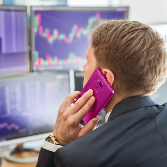 Image of man on mobile phone while in front of monitors
