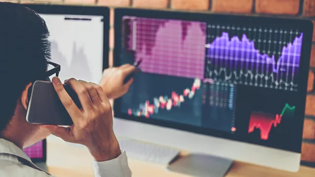 Image of man on phone while pointing at graphs in a monitor