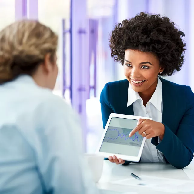Image of woman showing graph in a tablet to another woman