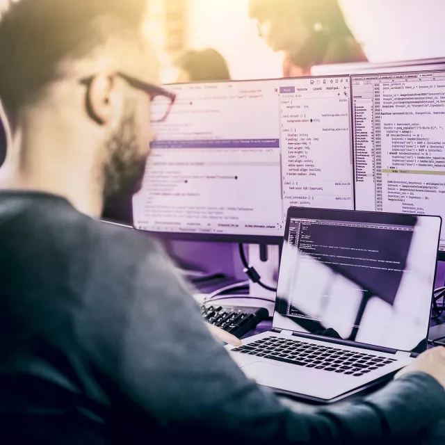 Image of man working on laptop with multiple monitors in an office