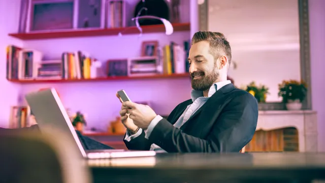 Image of man typing on phone with laptop open in desk