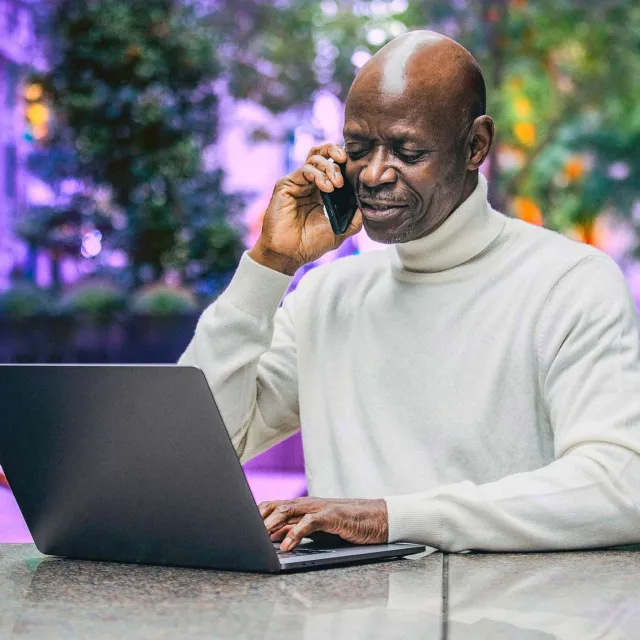 Image of man outdoors in a mobile phone call in front of laptop