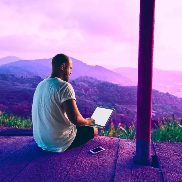 Image of man working on a laptop on high ground with a view of mountains