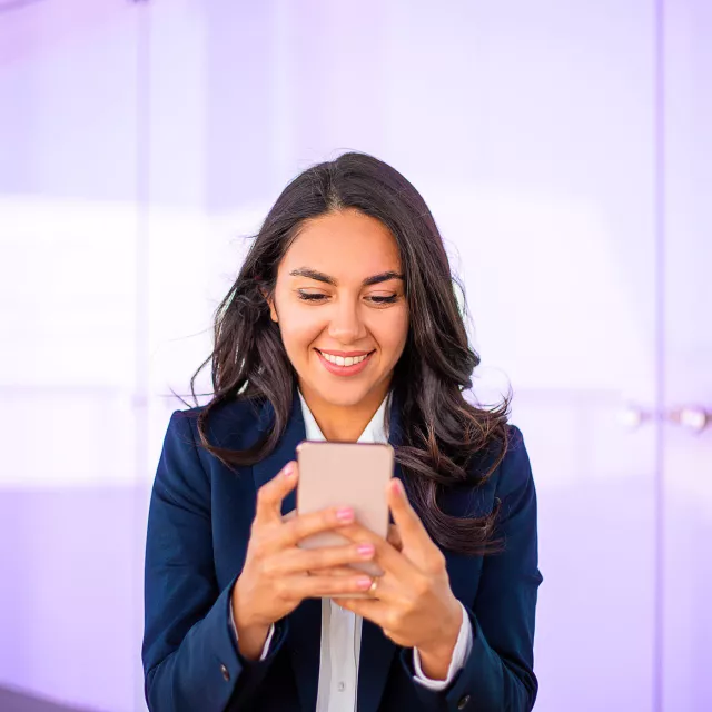 Person in a dark blue blazer holding a smartphone indoors near glass doors.