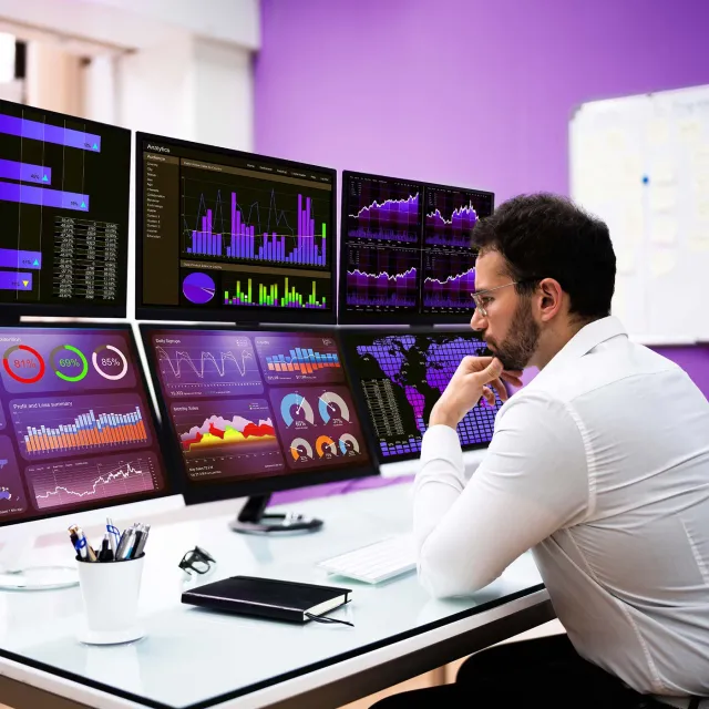 Person analyzing data visualizations on multiple computer monitors at a desk.