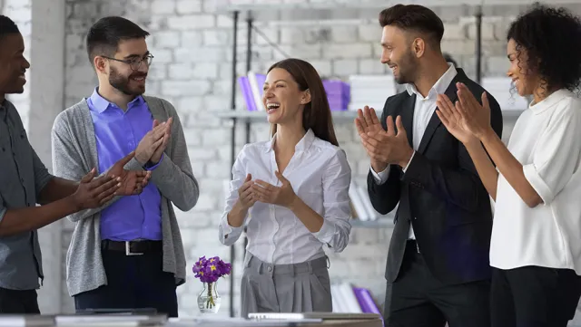 Diverse business team applauding in a modern office with brick walls and bookshelves.