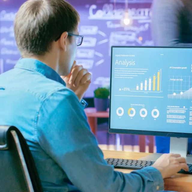 Business professional analyzing digital charts and sales data on a computer screen in a modern office setting.