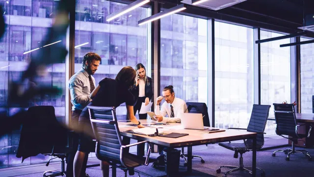 Business team meeting in a modern office with large windows overlooking a nearby building.