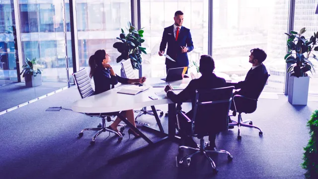Modern office meeting with professionals collaborating around a conference table in a city-view workspace.