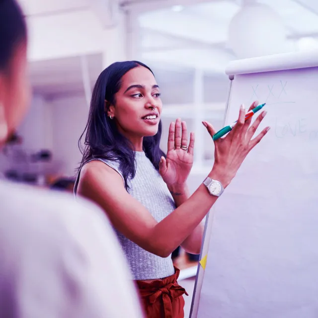 Woman leading a team meeting, writing on a flip chart in a modern office