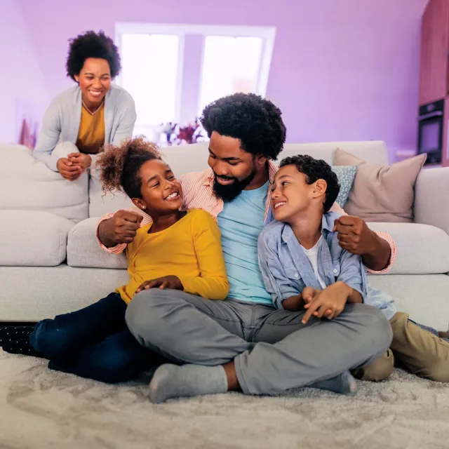 Family sitting together on a living room floor in front of a sofa, spending quality time in a cozy home environment.
