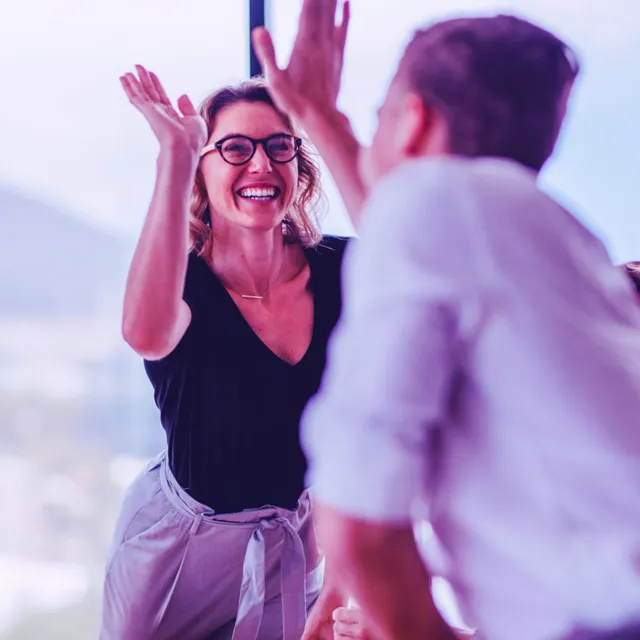 Business team in a modern office engaged in an animated discussion near large glass windows with a scenic mountain view in the background.
