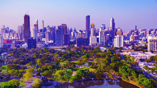 Bangkok city skyline with lush green park in the foreground under a clear blue sky.
