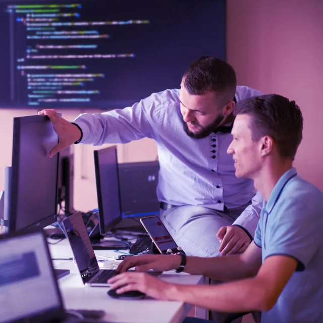 Developers collaborating on code review in a modern programming workspace with multiple monitors.
