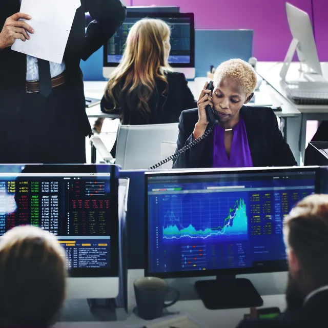 Financial analysts monitoring stock market data on multiple screens in a busy trading office.
