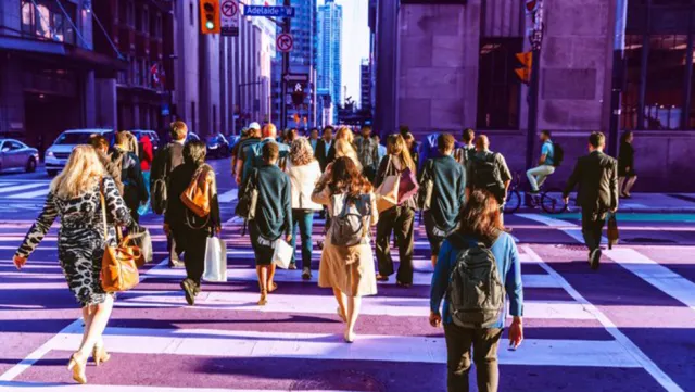 Crowd of people crossing a busy city street during rush hour in an urban downtown setting.