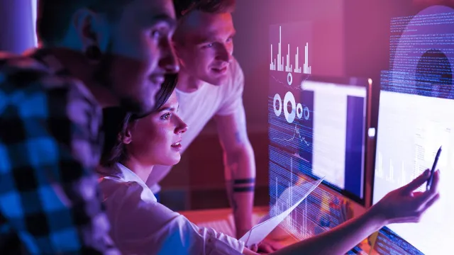 Team analyzing data and charts on digital screens in a modern tech-driven workspace.