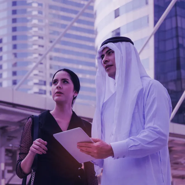 young handsome Arabian business man in white suit holding mobile tablet with secretary asian woman in modern city, financial, investment, teamwork, company success and business growth concept.