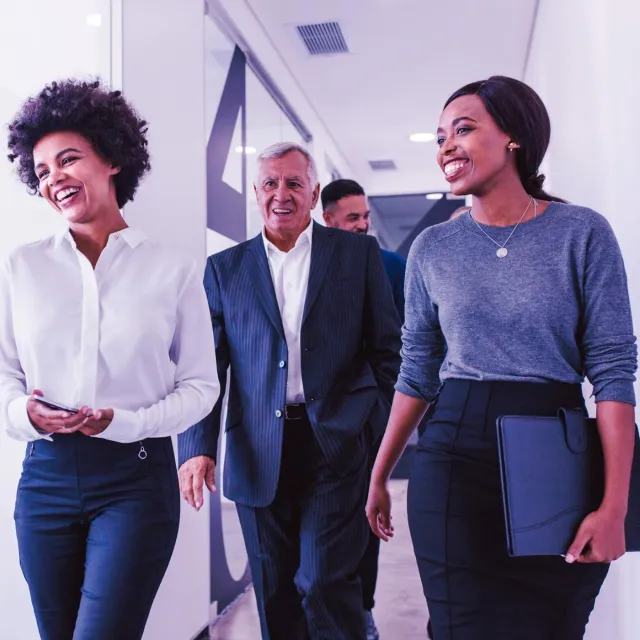 A group of business professionals walking in a modern office hallway.