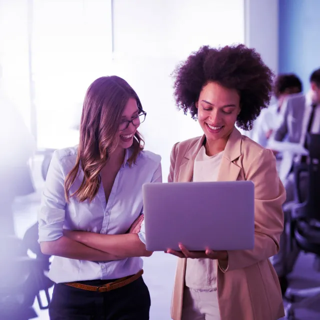 Two professionals standing in an office reviewing information on a laptop.