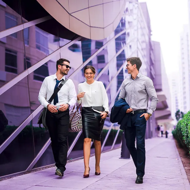 Three business professionals walking outside a modern glass office building.