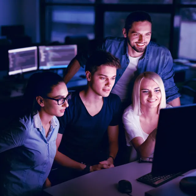 Team Of Programmers Working On Computer In Office. Young Beautiful People Working On Project Together In IT Office In Evening, Looking At Monitor, Sitting In Dark. Programming. High Resolution.