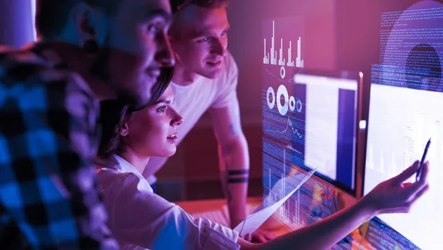 Colleagues analyzing interactive data dashboards and performance charts on a large digital display.