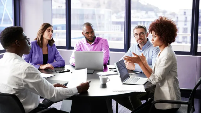 A team meeting around a conference table with laptops and documents.