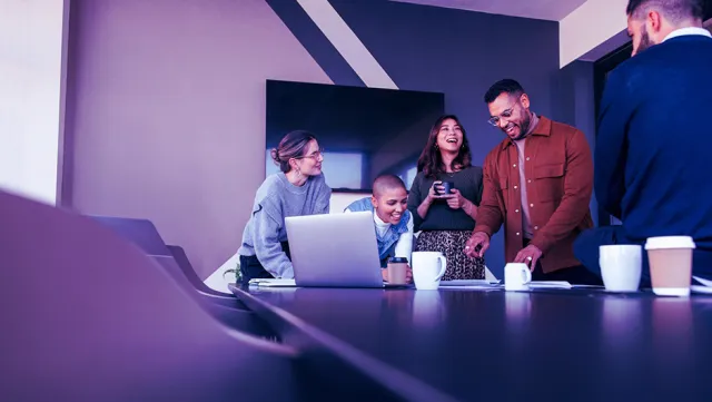 Team collaborating around a conference table with a laptop and documents during a meeting.