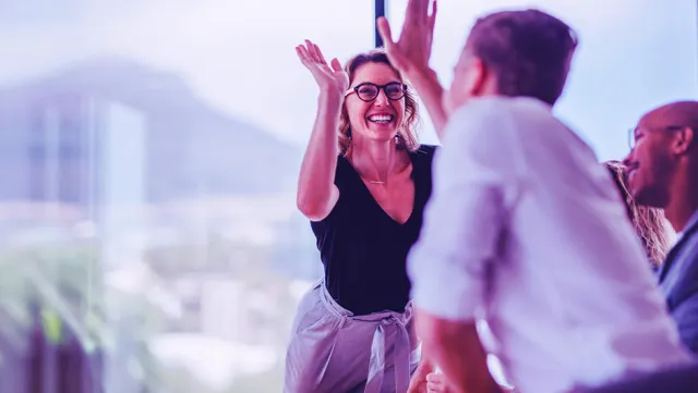 Business team in a modern office engaged in an animated discussion near large glass windows with a scenic mountain view in the background.