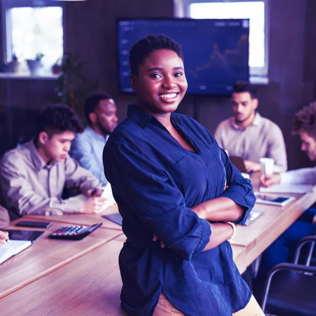 A person standing confidently in front of a team working at a conference table.