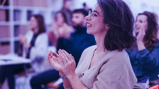 People seated in a classroom or seminar setting, attentively clapping during a session.