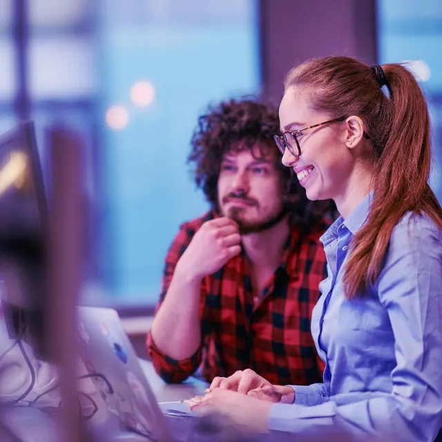 Business colleagues, a man and a woman, engage in discussing business strategies while attentively gazing at a computer monitor, epitomizing collaboration and innovation