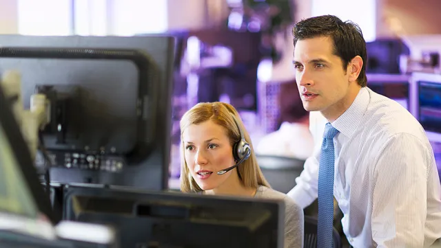 Supervisor guiding a call center agent at a multi‑monitor workstation