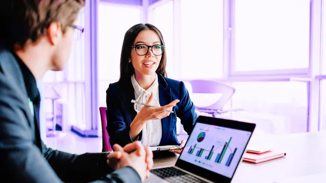 Image of woman explaining to man with laptop displaying graphs