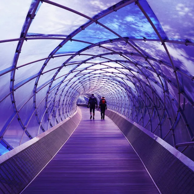 Two people walking through a modern, purple-lit tunnel.