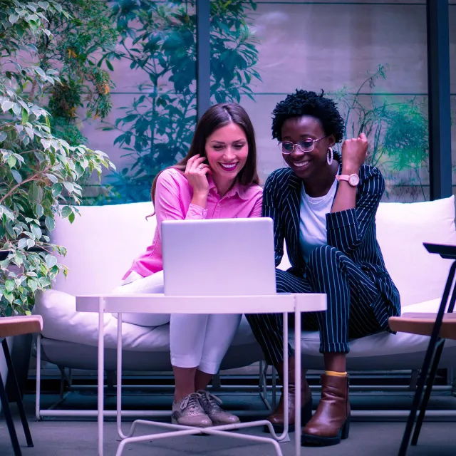 Image of two friends smiling while looking at a laptop