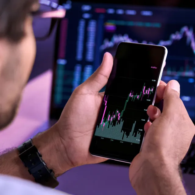 Image of man holding mobile phone displaying stock graph