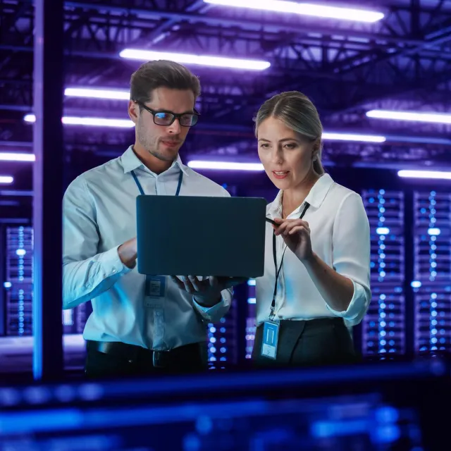Image of officemates discussing while holding a laptop in a mainframe room