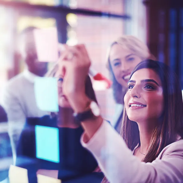 Team leader planning and writing on sticky notes while showing innovation, sharing a vision and ideas. Diverse group of creative office business people meeting together to market new startup company