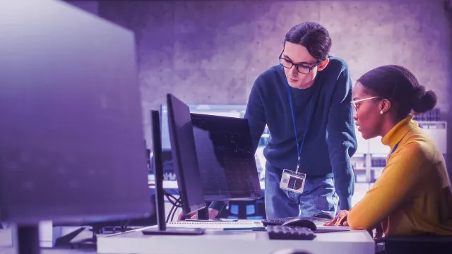 Image of two officemates looking at stocks graph in a monitor