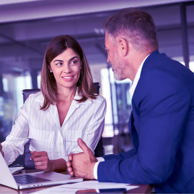Business professionals discussing project details at a laptop in a modern office.